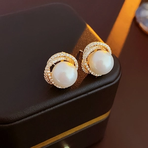 Close-up of gold pearl earrings with hollow zircon halo on a black jewelry box