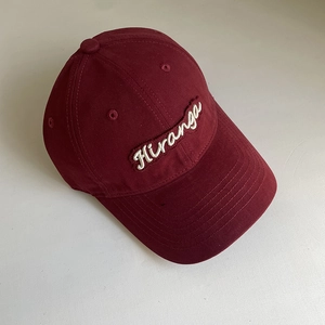 Detailed close-up of white Hiranga embroidery on a deep red cotton baseball cap