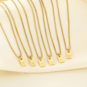 Macro shot of gold square initial pendants on box chains resting on luxury satin