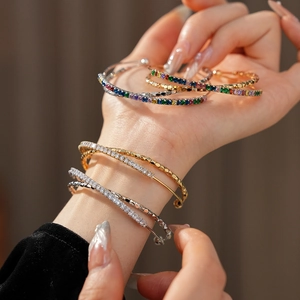 Close-up of stacked open bracelets with colorful zircons and refined diamond textures