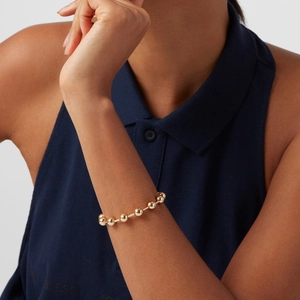 Gros plan d'un bracelet à perles dorées au poignet avec une finition métallique brillante