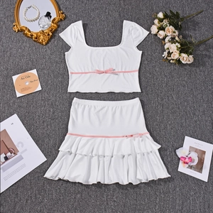Flat lay of white two-piece set with pink bow details and ruffled skirt on a textured rug