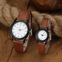 Close-up of minimalist couple quartz watches with brown leather straps on a wooden table