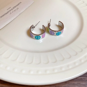 Detail view of C-shaped silver earrings with colorful smiley face enamel on a white plate
