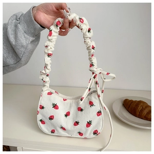 Close-up of white corduroy shoulder bag featuring red strawberry patterns and bow detail