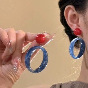 Detail of contrasting red stud and blue acrylic hoop earrings worn by a model