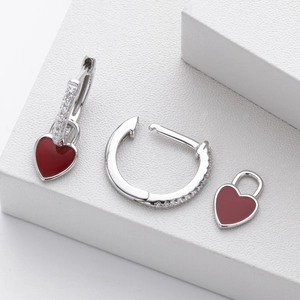 Macro detail of 925 sterling silver hoop earrings with red enamel heart pendants