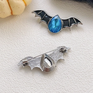 Halloween bat brooch with blue crystal and black enamel on a textured white surface