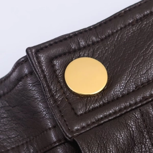Detalle macro del pantalón de cuero marrón oscuro con grano lichi y hebilla de metal dorado