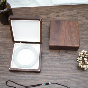 Detailed view of open walnut wood jewelry box with white bracelet inside on wooden table