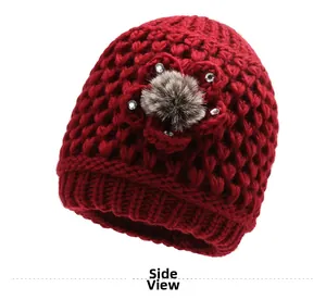 Detail view of red knitted hat featuring floral accents and a plush faux fur pompom