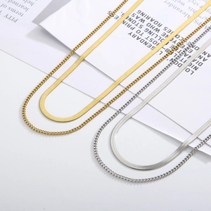 Flat lay of gold and silver layered snake chain and cuban link necklaces on white background