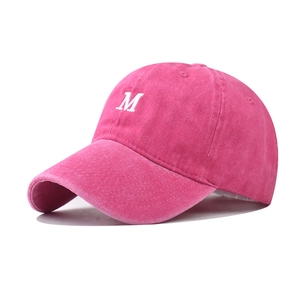 Macro detail of washed cotton fabric and white letter M embroidery on rose red baseball cap