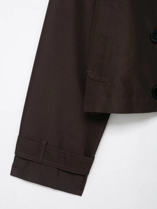 Detailed close-up of dark brown jacket cuff strap and side pocket with button detail