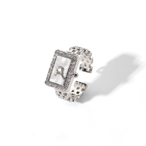 Détail d'une bague en forme de montre argentée avec cadran en nacre blanche et zircons