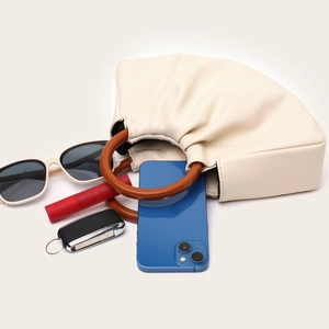 Interior storage of off-white pleated cloud bag with wooden handle and daily essentials