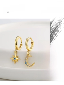 Close-up of gold star and moon earrings with blue and white zircon on white ceramic