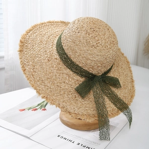 Detail of hand-woven straw hat with fringe brim and dark green lace bow decoration