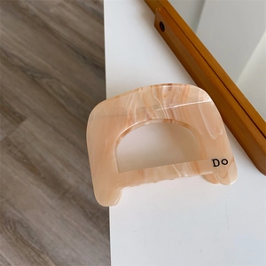 Macro shot of nude marble acetate hair claw featuring minimalist Do letter design