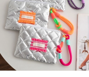 Detail of silver quilted makeup bag with colorful decorative patch and woven rope handle