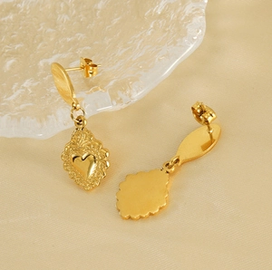 Detailed view of gold stainless steel sacred heart earrings on elegant silk fabric