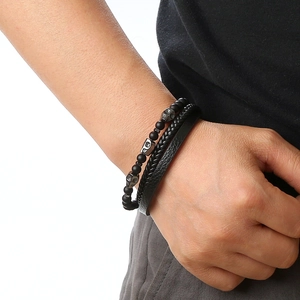 Detail of men's black leather braided bracelet and matte bead skull bracelet on wrist