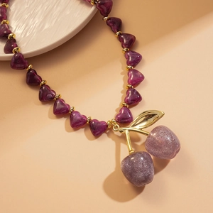 Close-up of a purple heart bead necklace featuring a sparkling cherry pendant on a ceramic plate
