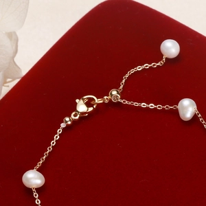 Elegant gold chain bracelet featuring lustrous white pearls on a deep red velvet backdrop