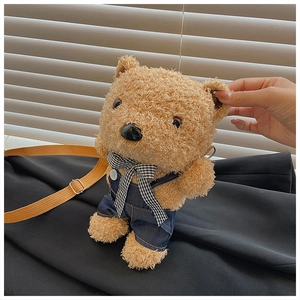 Detail of brown teddy bear plush crossbody bag wearing denim blue overalls and a bow
