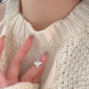Close-up of minimalist silver heart pendant necklace worn over a white knit sweater
