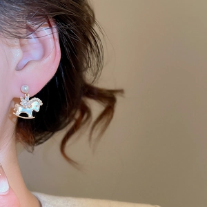 Close-up of gold plated rocking horse earrings with pearls and crystals on ear lobe