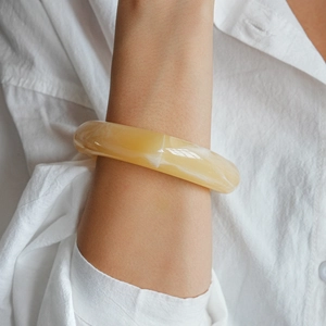 Detail of yellow marble texture acrylic cuff bracelet worn over a white linen sleeve