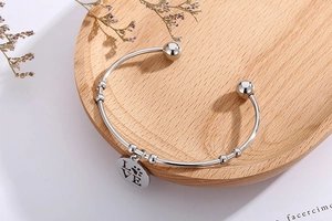 Detailed view of silver stainless steel cuff bracelet with LOVE pendant on wooden tray