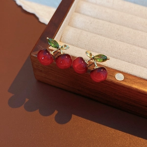 Macro shot of dark red resin cherry earrings with golden leaf details on a wooden box