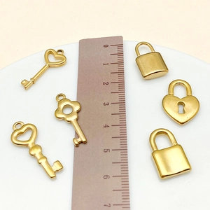 Golden stainless steel heart lock and key charms shown with ruler for size measurement