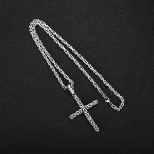 Close-up of silver cross pendant with Byzantine chain on a black textured background