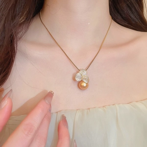 Close-up of gold-plated flower pendant with zircon petals and a large golden pearl necklace