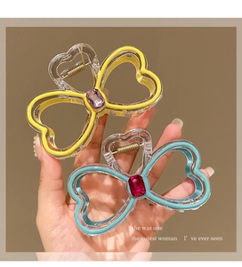 Detail of heart-shaped rhinestone bow hair claw clips in yellow and blue acrylic