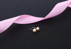 Macro shot of champagne pink pearl earrings on black texture with a pink ribbon detail