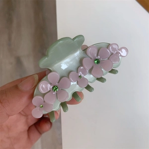 Close-up of light green acetate hair claw clip with pink floral patterns and rhinestones