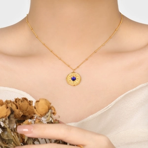 Elegant gold sunburst pendant necklace with blue gemstone on model with dried flowers