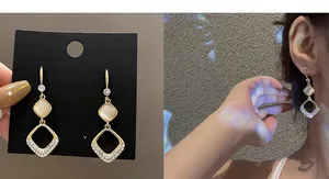 Detail of long gold tassel earrings with zircon and cat eye stone on model and card