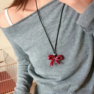 Gros plan d'un pendentif nœud en émail rouge sur cordon noir avec pull gris