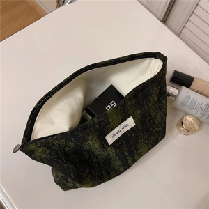 Macro view of textured green and black jacquard fabric makeup bag with simple wish label