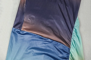 Detail of gradient satin dress showing shirred side seams and silk-like reflective texture