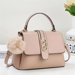 Close-up of pink textured leather handbag with gold hardware and plush pom-pom charm