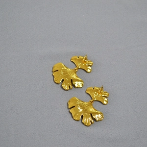 Macro shot of gold-plated ginkgo leaf earrings with layered texture and brushed finish