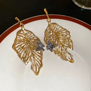 Golden hollow monstera leaf earrings with silver butterfly accent on a white ceramic plate