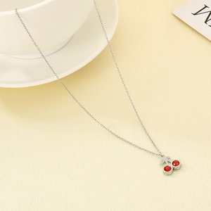 Detailed close-up of cherry pendant necklace with red stones on a minimalist background