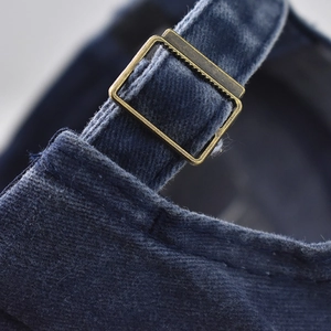 Macro shot of vintage bronze buckle and washed navy denim fabric on baseball cap back